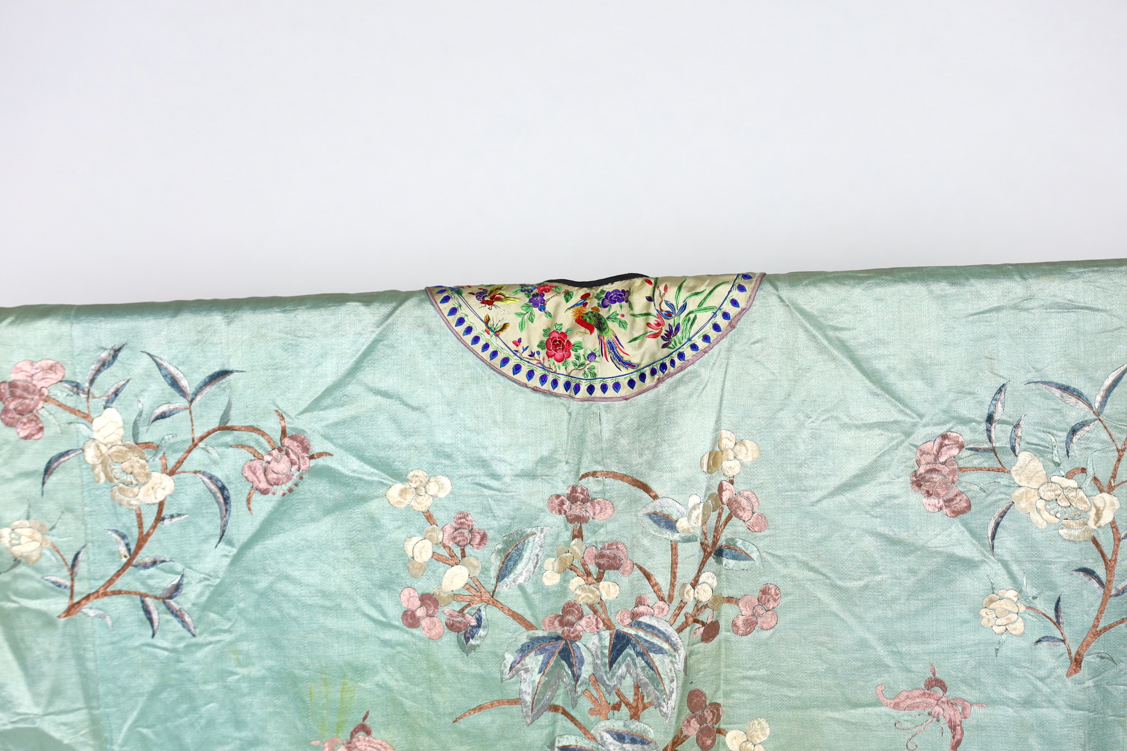 An early 20th century Chinese silk embroidered turquoise robe, embroidered in pastel silk with butterflies and flowers all over, polychrome embroidered braiding edged with lilac and bright pink sleeve bands embroidered w